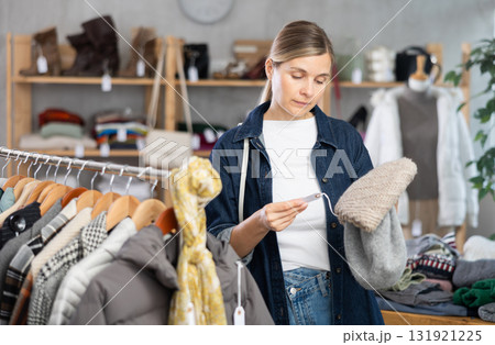 Focused european young woman choose hat for autumn-winter season in clothing store Focused european young woman choose hat for autumn-winter season in clothing store 131921225