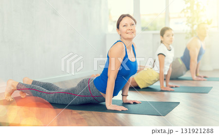 Happy middle-aged woman practicing cobra pose of yoga with her family 131921288