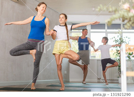 Friendly sporty parents with preteen daughter and son balancing in Vrikshasana or Tree position on gymnastic mats barefoot in yoga studio 131921290