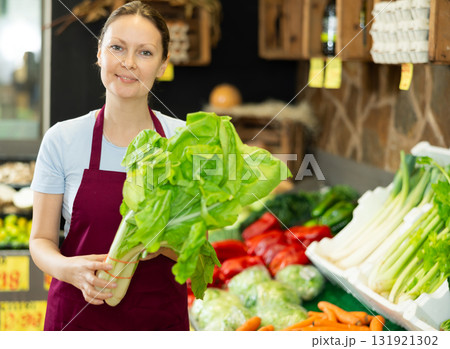 Woman seller of garden stuff store replenishing showcase, puts salad mangold on showcase 131921302