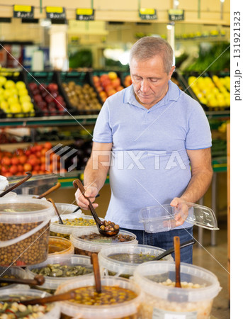 Elderly man purchaser putting olives into container in grocery store 131921323