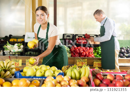 Girl seller of garden-stuff store works near showcase, sorting apples, checking goods Girl seller of garden-stuff store works near showcase, sorting apples, checking goods 131921355