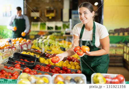 Young female seller wearing apron holding fresh tomatoes on market 131921356