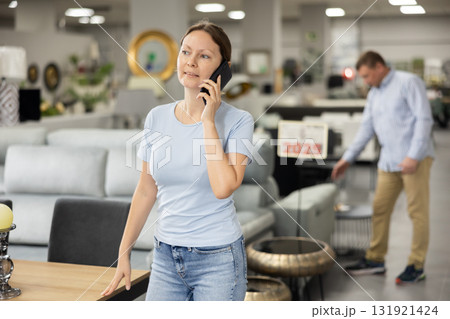Happy female customer in furniture store talks on phone and consults with spouse about purchase Happy female customer in furniture store talks on phone and consults with spouse about purchase 131921424