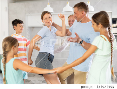 Children stand around their dancing parents in kitchen. 131921453