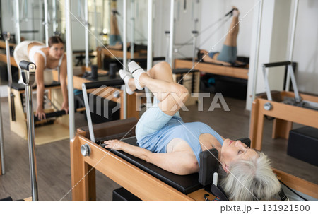 Senior woman doing stretching exercises on pilates reformer Senior woman doing stretching exercises on pilates reformer 131921500