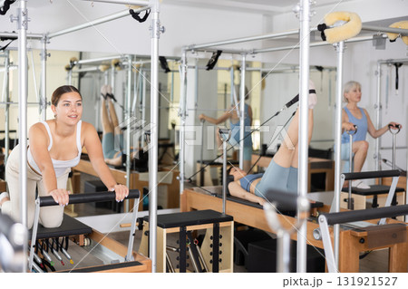Positive young girl practicing pilates stretching exercises on reformer at gym 131921527