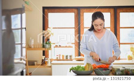 Adult woman slicing fresh carrots on wooden cutting board while preparing vegetables for weekly meal prep Adult woman slicing fresh carrots on wooden cutting board while preparing vegetables for weekly meal prep 131921750