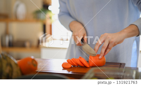 Adult woman slicing fresh carrots on wooden cutting board while preparing vegetables for weekly meal prep 131921763