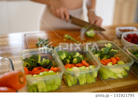 Woman preparing fresh vegetables for healthy meal prep, organizing colorful ingredients in containers 131921795