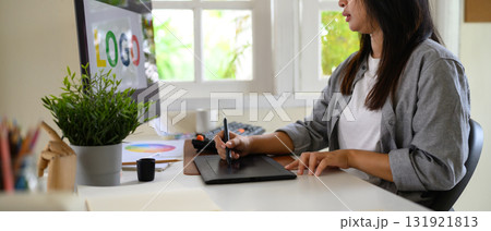 Graphic designer using drawing tablet and computer to create colorful logo in bright modern workspace 131921813