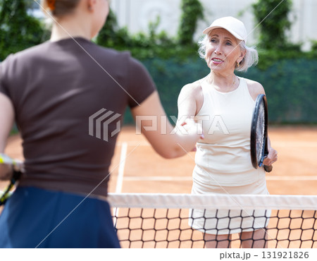 Young and senior women tennis players shake hands across net. 131921826