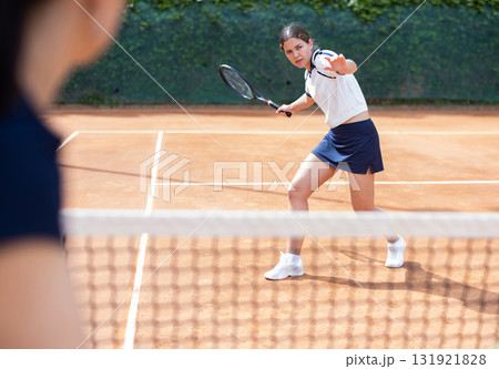 Girl plays tennis on open court with opponent 131921828