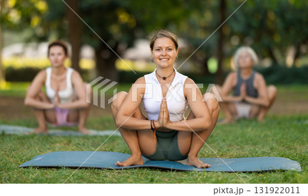 Girl performing Garland Pose during group yoga in park 131922011