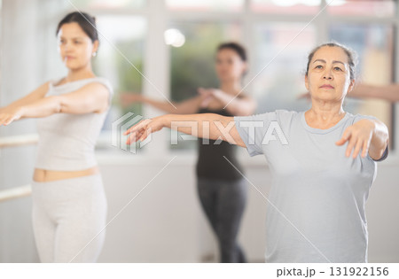 Graceful women of different ages practice various ballet movements in choreographic studio Graceful women of different ages practice various ballet movements in choreographic studio 131922156