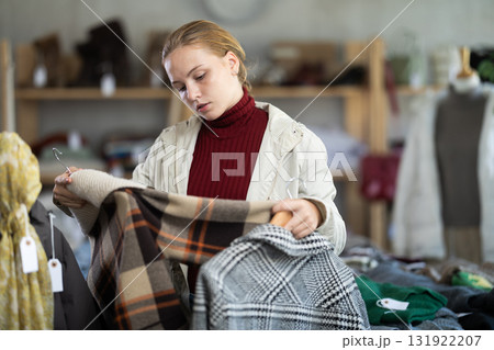 Attentive teenage girl choosing something for autumn-winter in clothing store 131922207