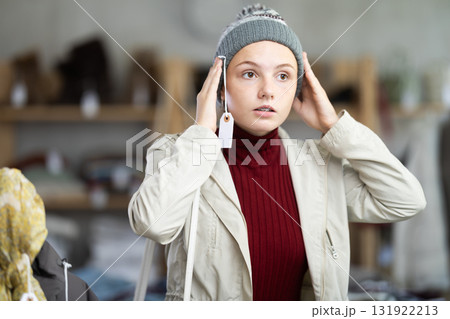 Girl is fitting on and trying on warm hat in store Girl is fitting on and trying on warm hat in store 131922213