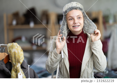 Positive teenage girl trying fur hat in clothing store Positive teenage girl trying fur hat in clothing store 131922219