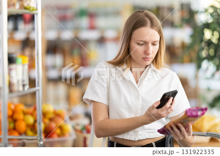 Checking expiration date of spaghetti - female shopper scans QR code on label of spaghetti using smartphone 131922335
