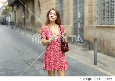 Young woman in summer dress standing on street with phone in hands 131922362