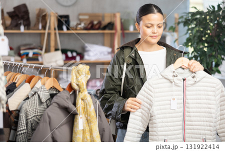 Asian woman standing in clothing shop and looking new down jacket made of high-quality material. Shopping and seasonal sales concept, autumn-winter season 131922414