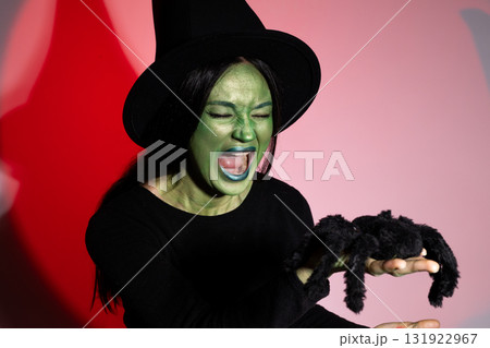 Woman in witch costume holding stuffed spider at Halloween party 131922967