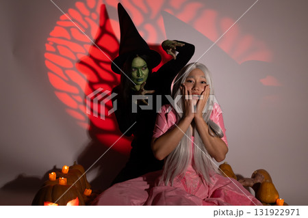 Woman in pink dress with witch costume laughing in front of Halloween decoration Woman in pink dress with witch costume laughing in front of Halloween decoration 131922971