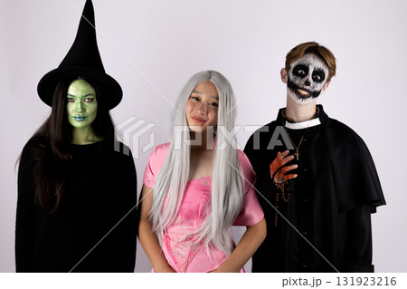 Three people in Halloween costumes, including a witch, a ghost, and a skeleton 131923216