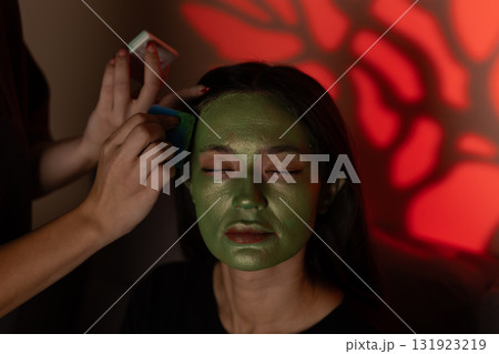 The model is getting her face painted green for a Halloween costume 131923219