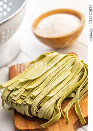 Green tagliatelle pasta on cutting board on white table. Green tagliatelle pasta on cutting board on white table. 131923659