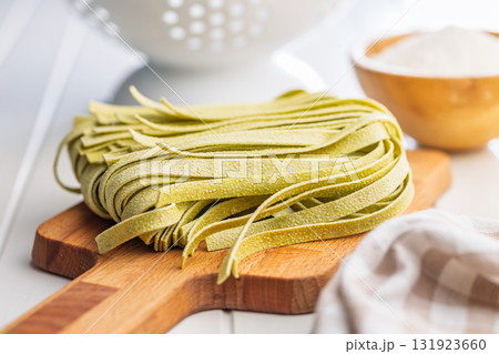 Green tagliatelle pasta on cutting board on white table. Green tagliatelle pasta on cutting board on white table. 131923660