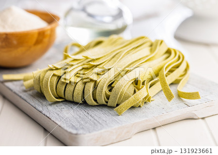 Green tagliatelle pasta on cutting board on white table. 131923661