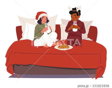 Cute girl and boy wearing traditional Christmas pajamas eating gingerbread cookies sitting on bed 131923856