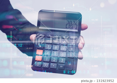 Hand holding a calculator displaying 2025 against a background of financial data and stock market charts. Concept economic forecasts and business predictions for the year 2025. 131923952