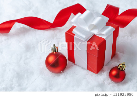 A festive gift box with red ornaments against a snowy background adds to seasonal joy A festive gift box with red ornaments against a snowy background adds to seasonal joy 131923980