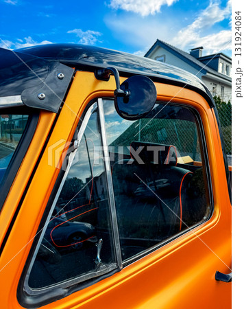 Classic orange vehicle with a unique side mirror captured against a clear blue sky in a suburban area during daytime Classic orange vehicle with a unique side mirror captured against a clear blue sky in a suburban area during daytime 131924084