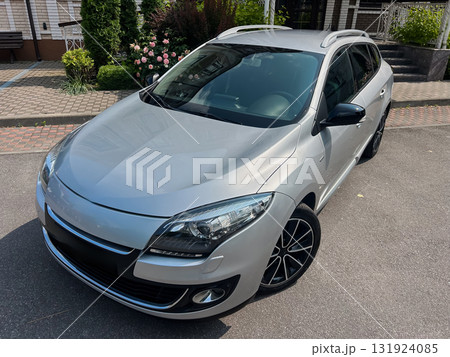 A sleek, shiny silver hatchback is parked stylishly amidst a vibrant and modern urban environment, showcasing its design and performance in a cityscape filled with life and innovation 131924085