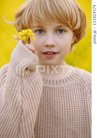 Blonde girl holding yellow flower near face in beige sweater, front view Blonde girl holding yellow flower near face in beige sweater, front view 131924374