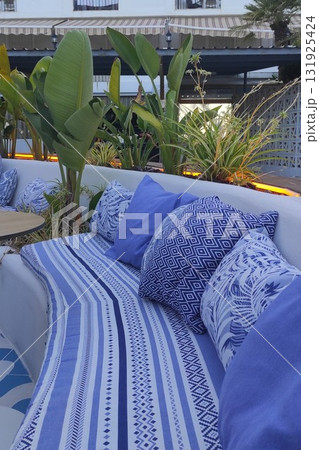 Cozy outdoor seating area featuring blue patterned cushions and lush greenery, creating a serene atmosphere for relaxation and social gatherings in a stylish environment Cozy outdoor seating area featuring blue patterned cushions and lush greenery, creating a serene atmosphere for relaxation and social gatherings in a stylish environment 131925424