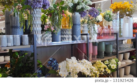 Colorful display of various flower arrangements in decorative vases on shelves, showcasing vibrant floral designs and textures in a modern retail environment Colorful display of various flower arrangements in decorative vases on shelves, showcasing vibrant floral designs and textures in a modern retail environment 131925426