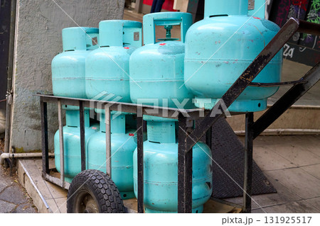 A cart loaded with multiple turquoise propane tanks, ready for delivery or service, placed on a city street. They are stacked neatly. A cart loaded with multiple turquoise propane tanks, ready for delivery or service, placed on a city street. They are stacked neatly. 131925517