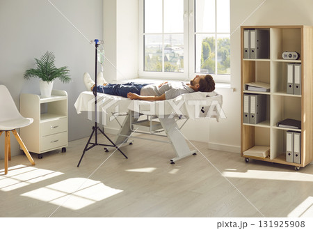 Man lying on the couch in clinic and receiving IV drip infusion and vitamin therapy. 131925908