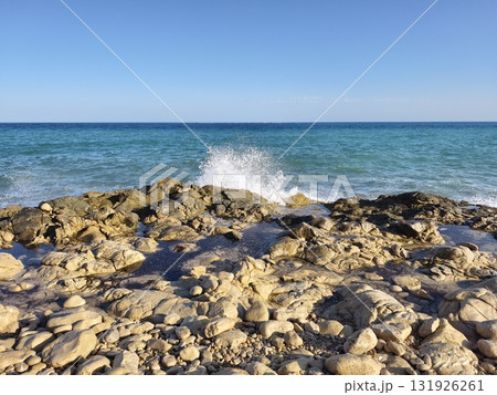 Experience the serene coastal view with waves gently crashing on the rocky shoreline 131926261