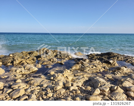 A serene coastal landscape showcases the clear blue ocean alongside a rugged rocky shoreline 131926267