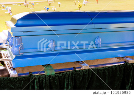 Casket at bright blue surrounded by flowers, attendees at memorial service in peaceful cemetery Casket at bright blue surrounded by flowers, attendees at memorial service in peaceful cemetery 131926986