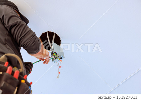 An electrician works on installing new light fixture inside ceiling, focusing on wiring connections. 131927013
