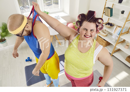Funny, happy, fat, strong woman holding her exhausted personal trainer by his sleeveless shirt 131927371