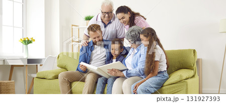 Happy family parents, kids, grandparents look at family photo album together sit in living room. 131927393