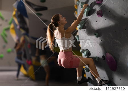 Girl climbs artificial wall bouldering, working out in gym 131927860