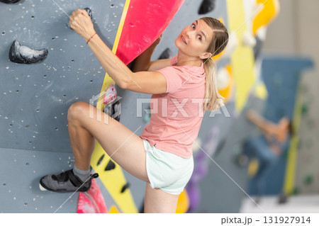 Woman climbs artificial wall bouldering, working out in gym Woman climbs artificial wall bouldering, working out in gym 131927914